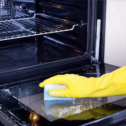 Woman cleaning oven. Close up of female hand with yellow protective gloves cleaning oven door